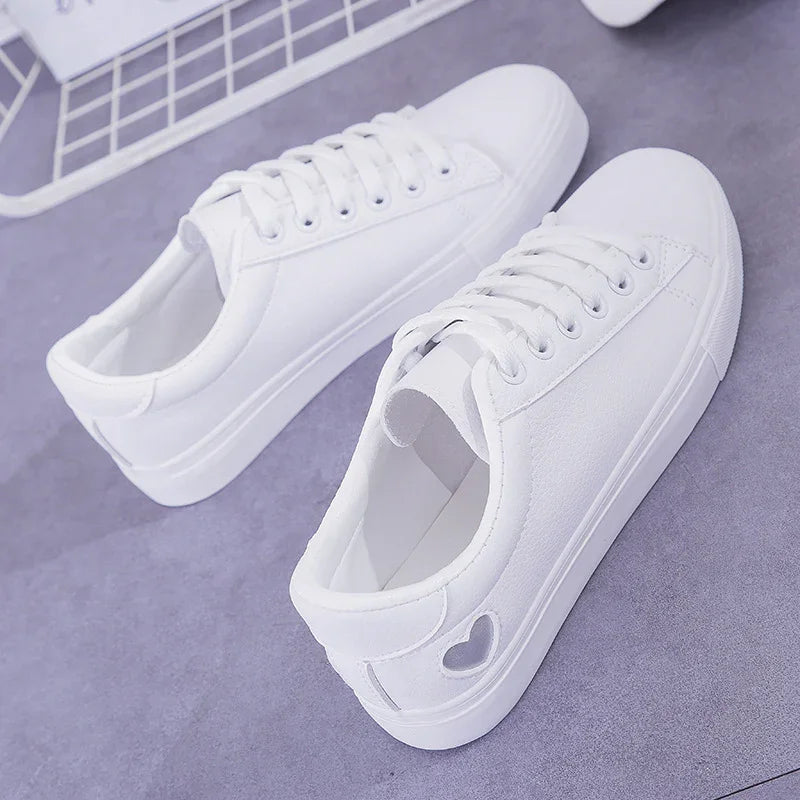 Pair of white canvas sneakers with lace-up design and heart cutout detail on gray surface