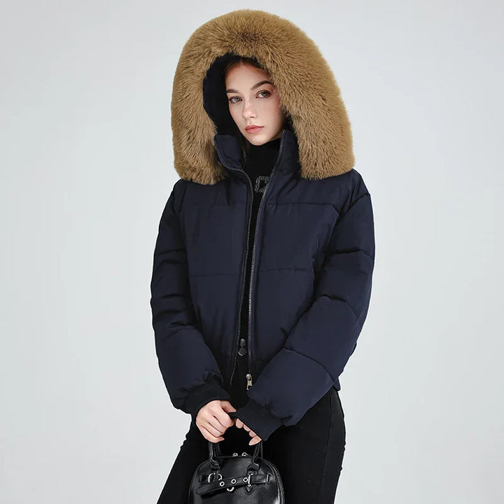 Woman wearing a black puffer jacket with large brown fur hood holding a black handbag