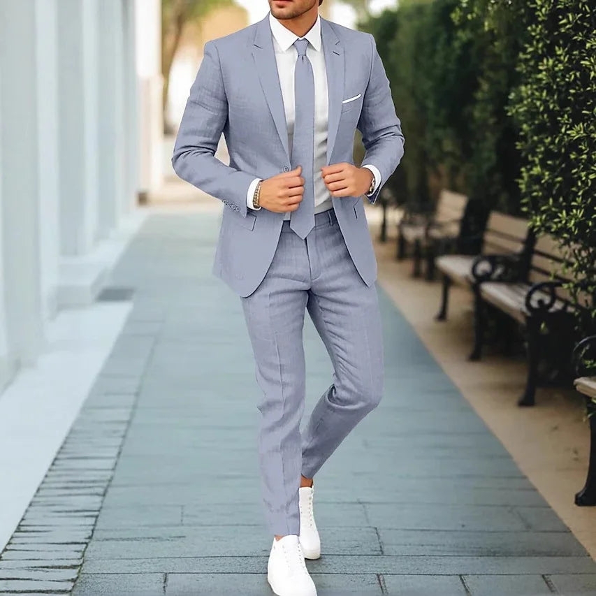 Man wearing light blue slim fit suit with tie and white sneakers walking outdoors on paved path