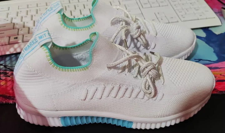 White knit athletic shoes with light blue accents and textured sole placed on a colorful surface with a keyboard in background