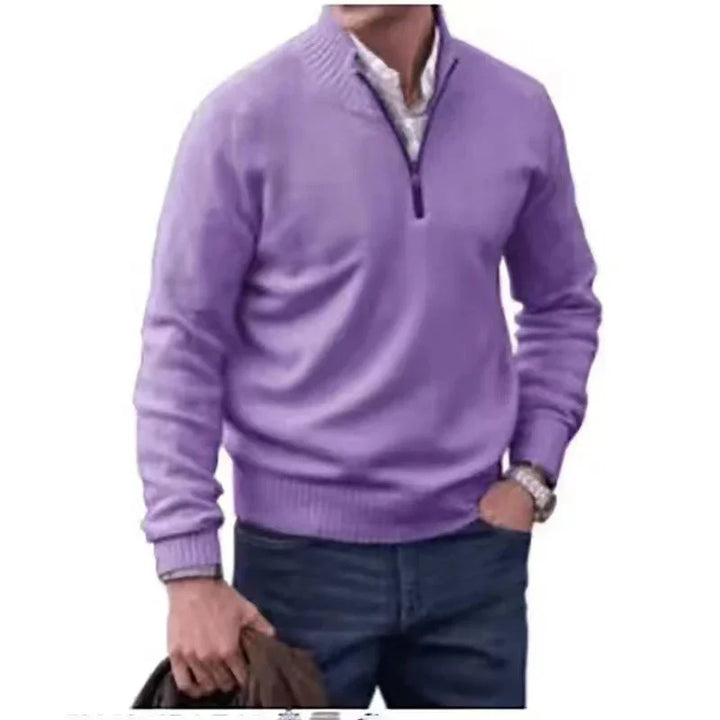 man wearing purple quarter-zip sweater over white shirt with blue jeans holding brown jacket