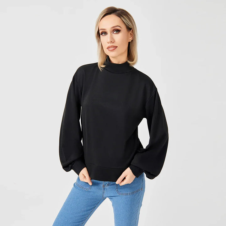 Blonde woman wearing black long-sleeve mock neck sweatshirt and blue jeans on white background