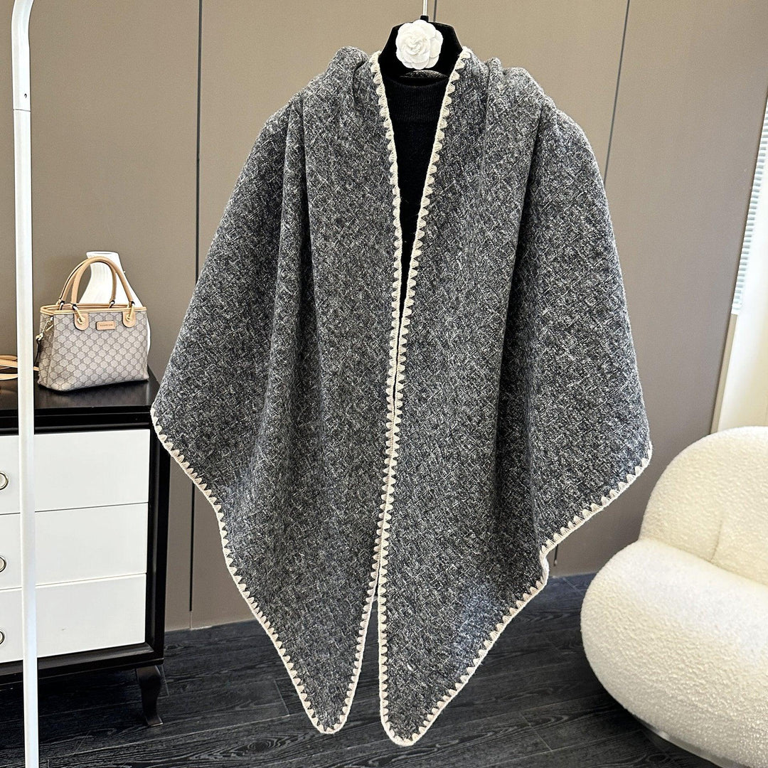 Gray textured knit wool poncho with white trim displayed on black mannequin in modern room