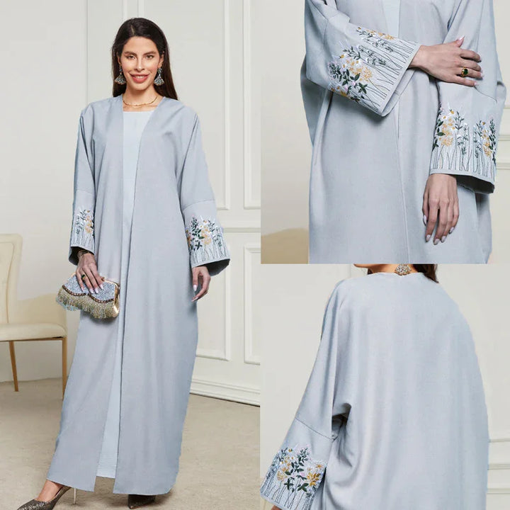 Woman wearing light blue abaya with floral embroidery on wide sleeves, holding embellished clutch