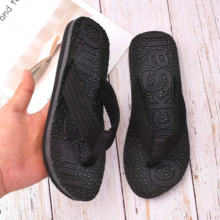 Close-up of black QuickSeal flip-flops with textured soles on white wooden floor