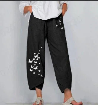 Woman wearing black wide-leg pants with white butterfly prints and a white top, barefoot on a gray background