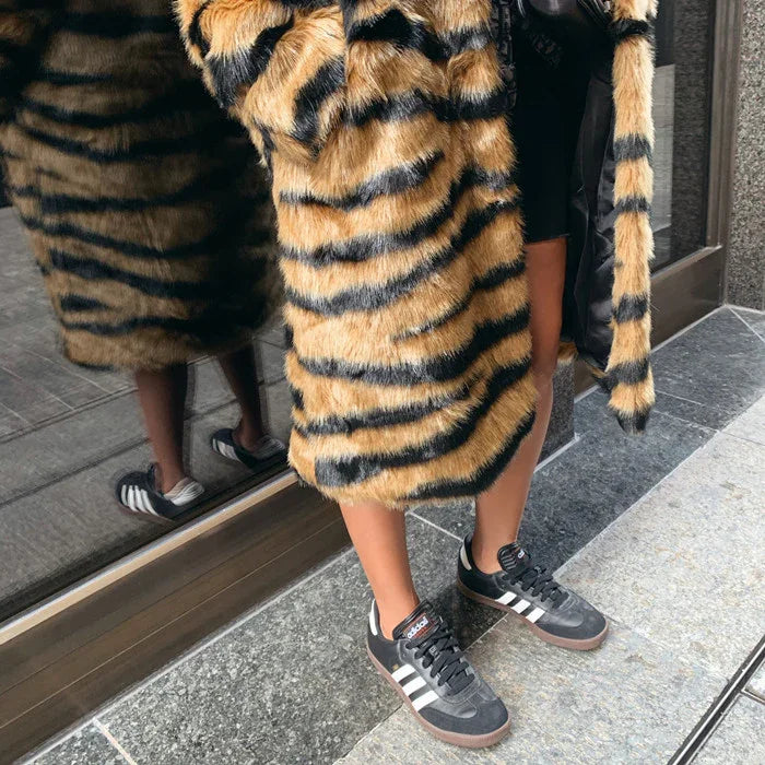 person wearing tiger-striped faux fur coat and black Adidas sneakers standing on stone pavement