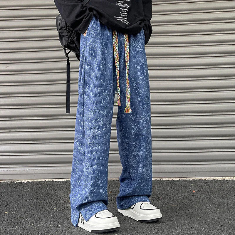 Person wearing blue textured wide-leg pants with colorful drawstrings and white sneakers against a metal shutter