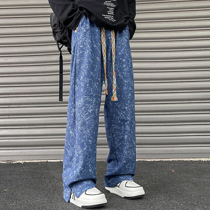 Person wearing blue textured wide-leg pants with colorful drawstrings and white sneakers against a metal shutter
