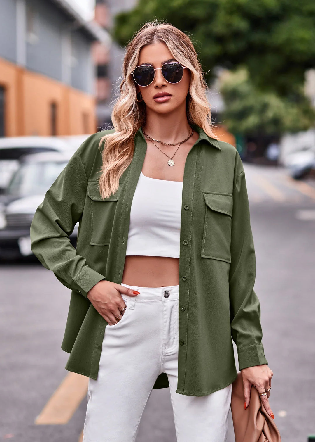 Blonde woman wearing oversized olive green shirt jacket, white crop top and pants, sunglasses, street background