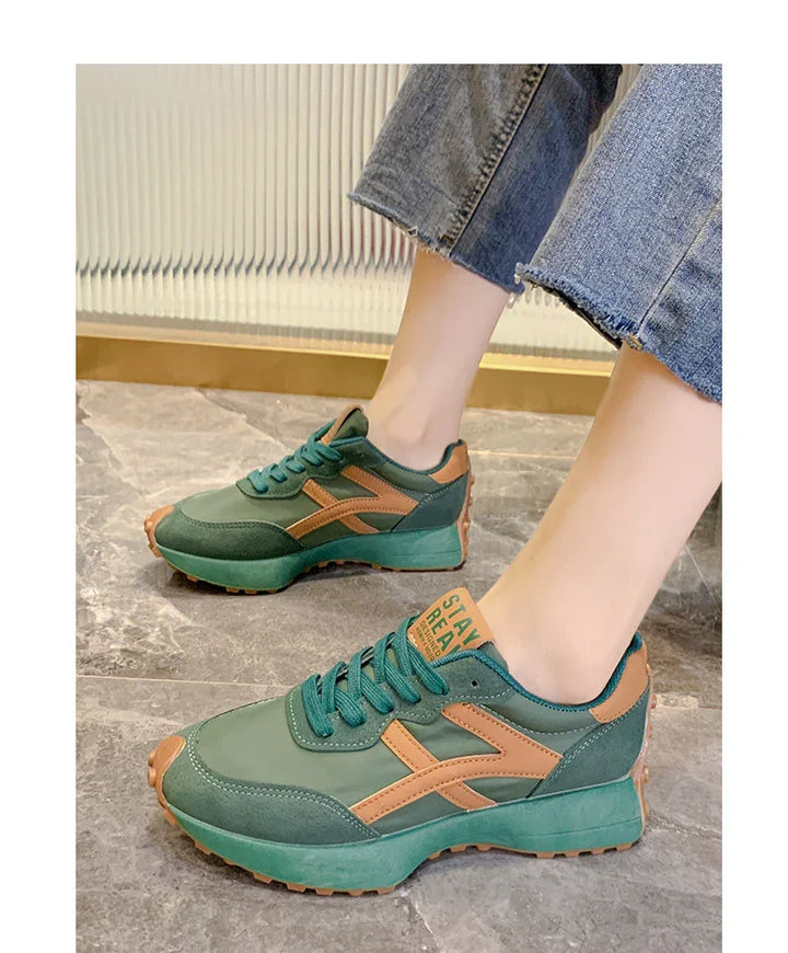 Green and tan casual sneakers with laces worn with cropped blue jeans on tiled floor