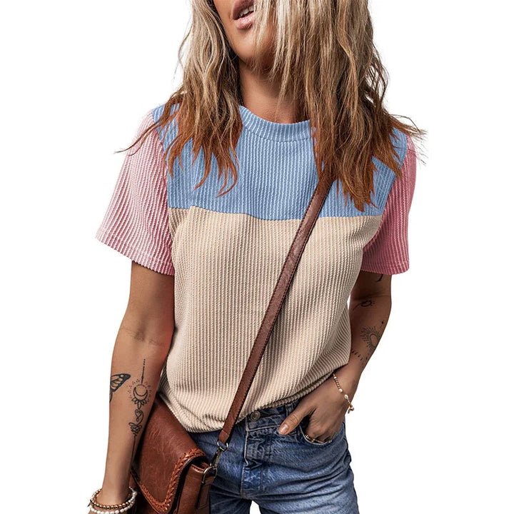 Woman wearing ribbed short-sleeve colorblock knit top in blue, beige, and pink, with brown crossbody bag and tattoos