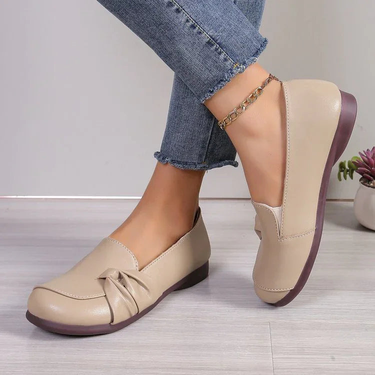 Beige leather flat shoes with a decorative bow detail worn with blue rolled-up jeans and gold ankle bracelet