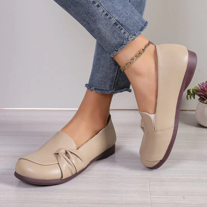 Beige leather flat shoes with a decorative bow detail worn with blue rolled-up jeans and gold ankle bracelet