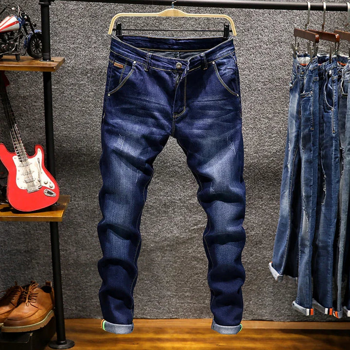 Dark blue denim jeans hanging on a wooden hanger with faded details, displayed in a clothing store