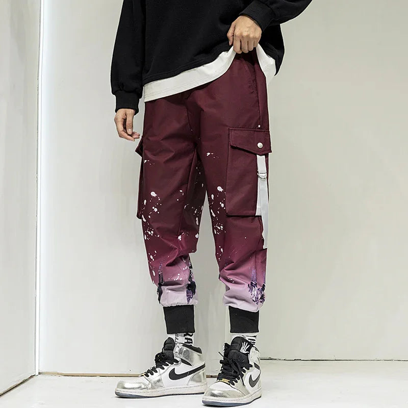 Man wearing maroon cargo pants with white paint splatter and graphic cuffs, paired with silver Nike sneakers