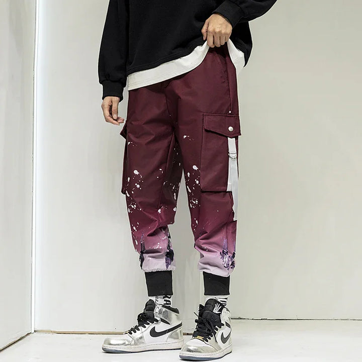 Man wearing maroon cargo pants with white paint splatter and graphic cuffs, paired with silver Nike sneakers