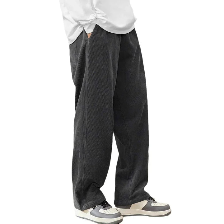 Person wearing loose black corduroy pants paired with white and gray sneakers and a white shirt