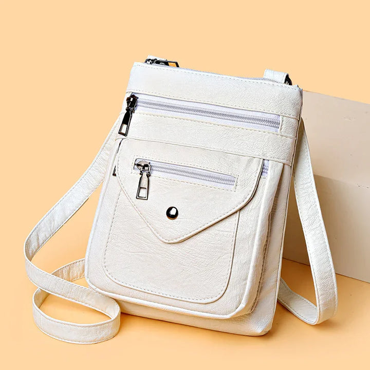 White crossbody bag with zipper pockets and adjustable strap on beige background
