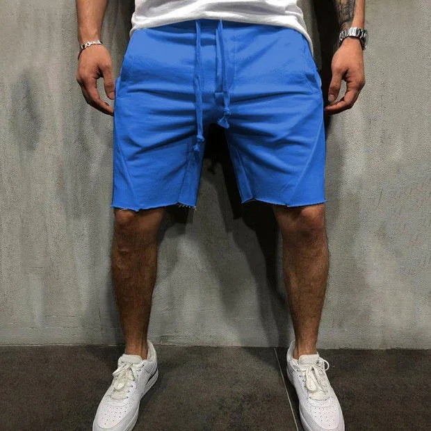 Man wearing bright blue casual shorts with drawstring waist and white sneakers against gray wall
