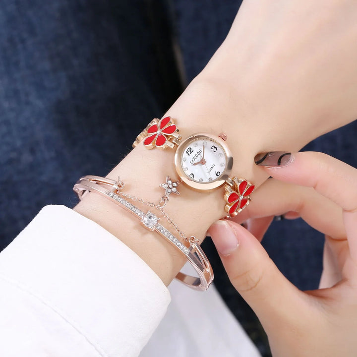 Rose gold wristwatch with red flower charms and a crystal bracelet on a woman's wrist