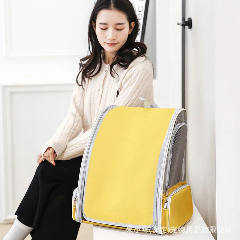 Woman sitting beside a yellow and gray pet carrier backpack in a bright room