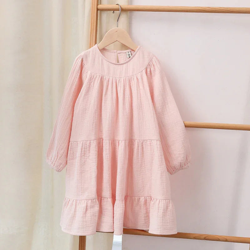 Soft pink long sleeve toddler dress with gathered tiers, hanging on wooden rack