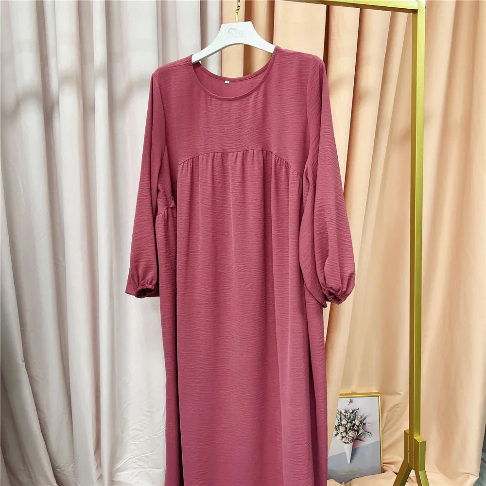 Mauve long sleeve loose dress with gathered detail hanging on white hanger against beige curtains