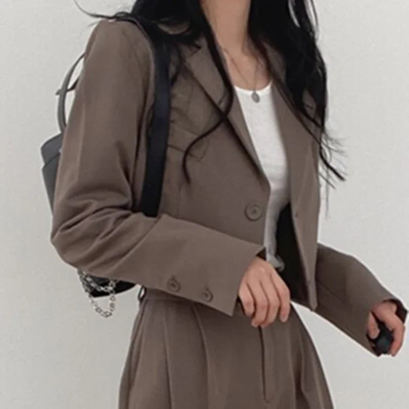 Woman wearing brown cropped blazer and matching high-waist pants with white top and black backpack