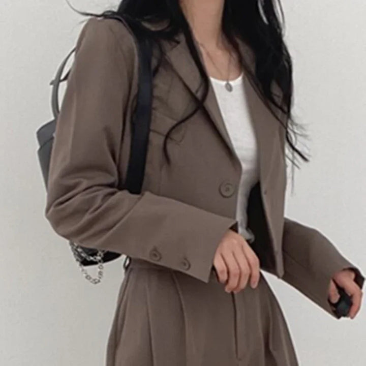 Woman wearing brown cropped blazer and matching high-waist pants with white top and black backpack