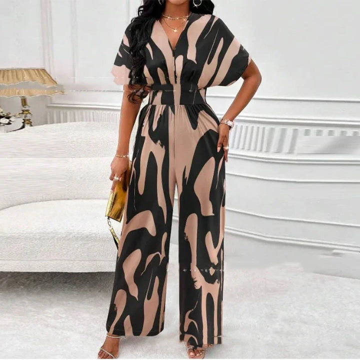 Woman in stylish black and beige abstract print jumpsuit with wide leg pants, holding gold clutch