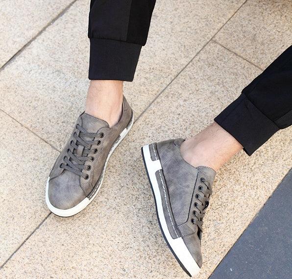 Casual gray leather sneakers with white soles worn with black pants on tiled floor