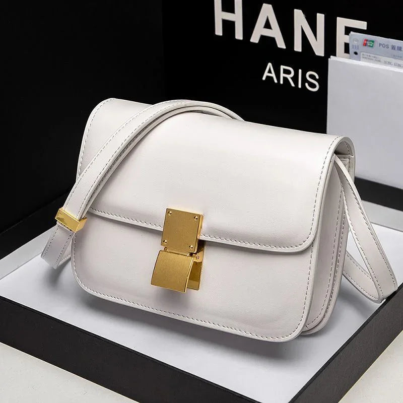 White leather crossbody handbag with gold clasp and adjustable strap on black and white background