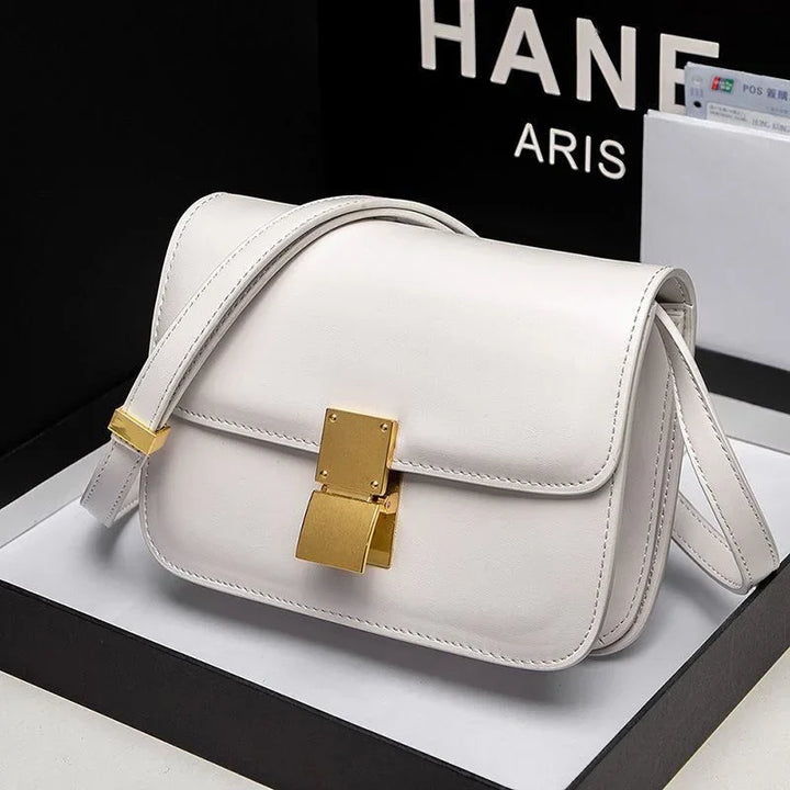 White leather crossbody handbag with gold clasp and adjustable strap on black and white background