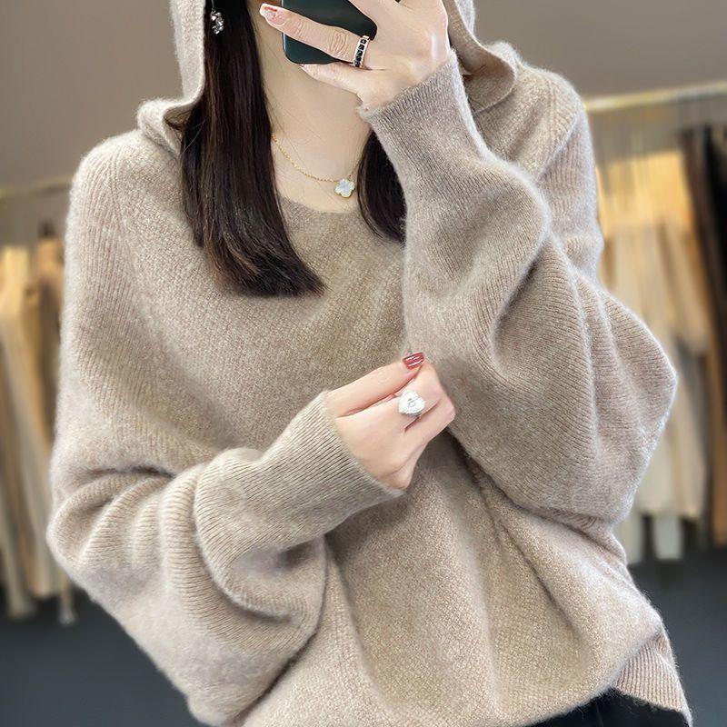 Woman wearing cozy beige hooded sweater with long sleeves, gold necklace, and silver ring taking a selfie