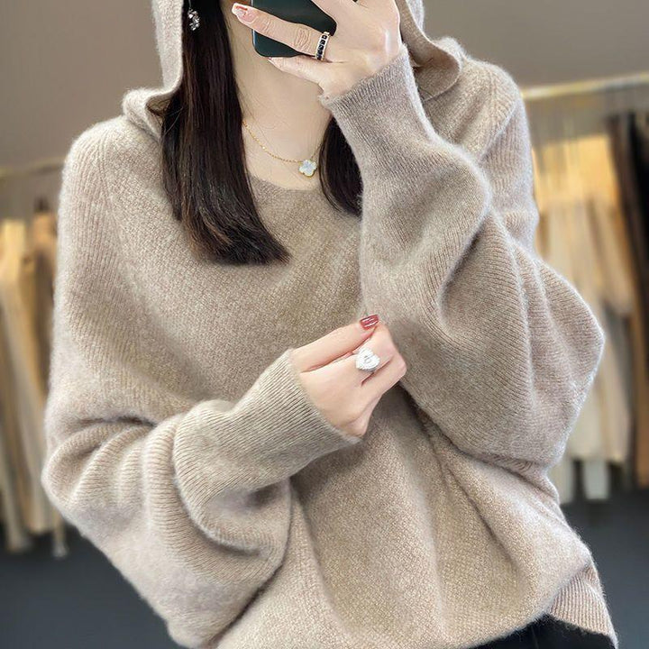 Woman wearing cozy beige hooded sweater with long sleeves, gold necklace, and silver ring taking a selfie