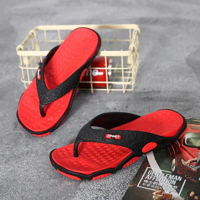 Red and black sport flip-flops on gray surface with wire basket and magazine nearby