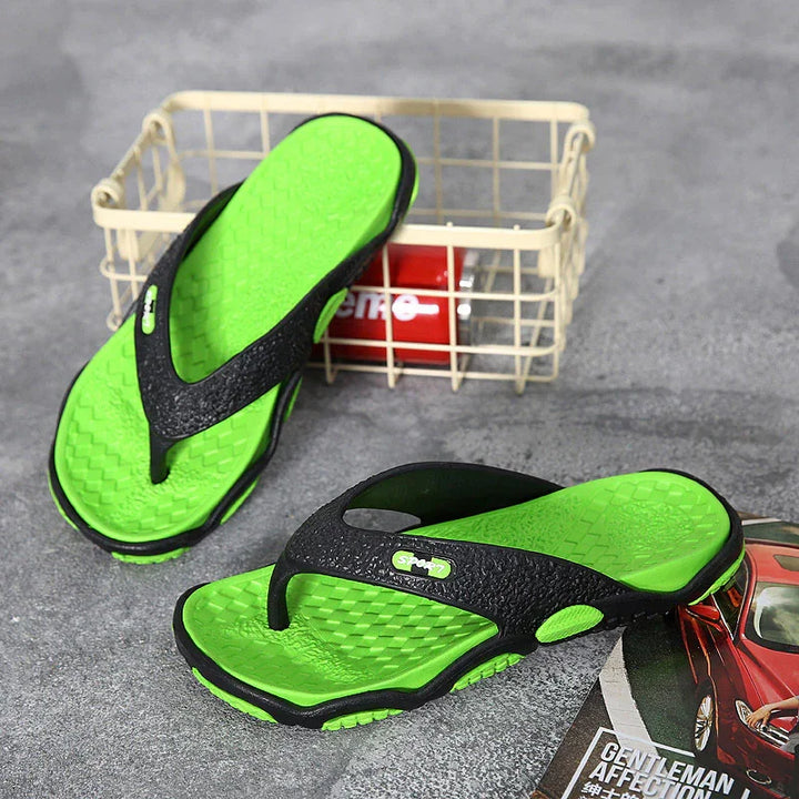 Green and black sport flip-flops on gray surface with metal basket and magazine