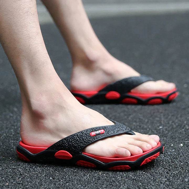 Feet wearing black and red sporty flip-flops on asphalt ground