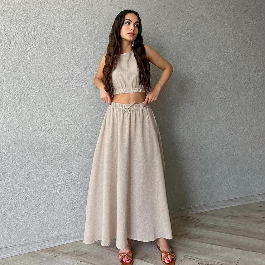 Woman in beige crop top and long skirt standing against gray textured wall on wooden floor