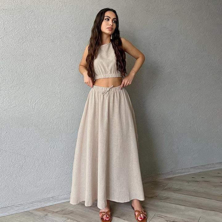 Woman in beige crop top and long skirt standing against gray textured wall on wooden floor