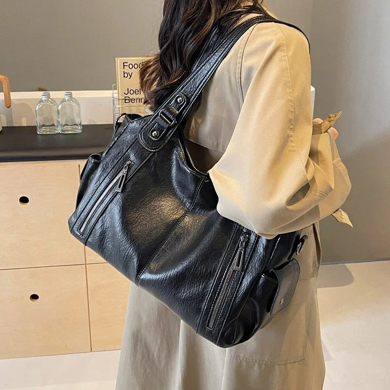 Woman wearing beige coat carrying stylish black leather shoulder bag with zipper pockets indoors