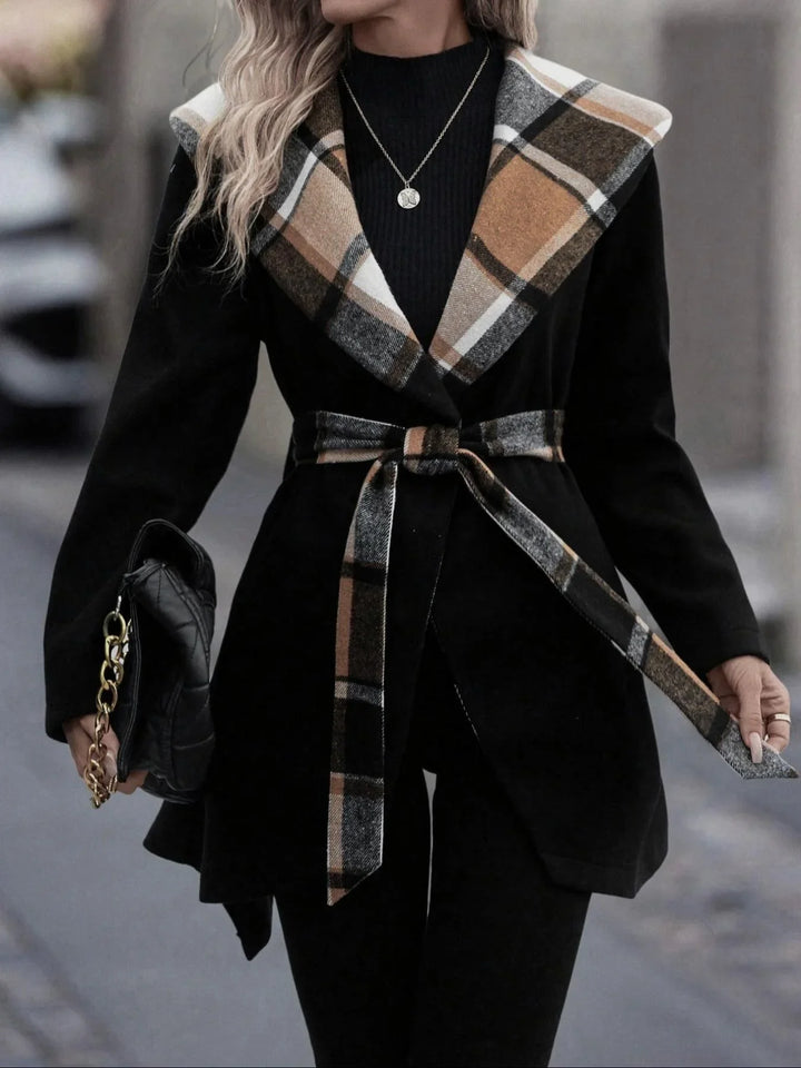Woman wearing black coat with brown plaid collar and belt, holding black handbag with gold chain