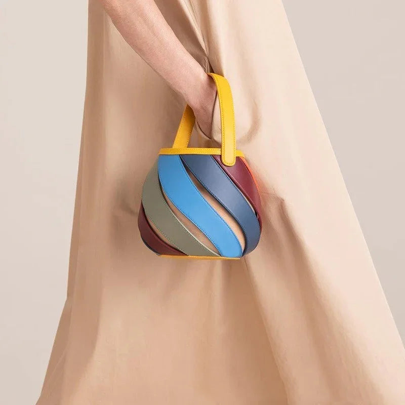Hand holding a small multicolor handbag with yellow handle, beige dress background