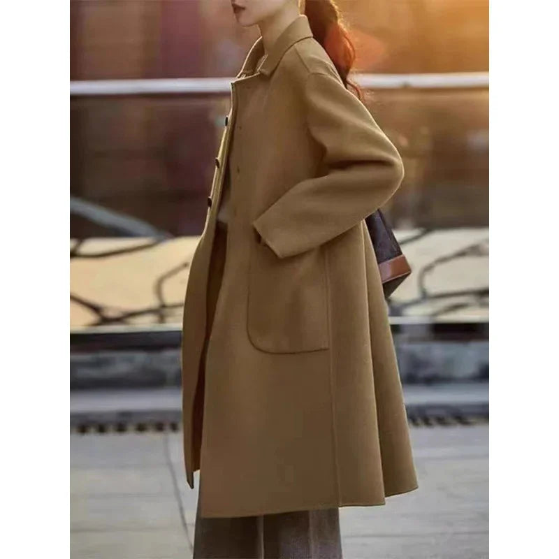Woman wearing stylish camel brown wool coat outdoors at sunset with hands in pockets