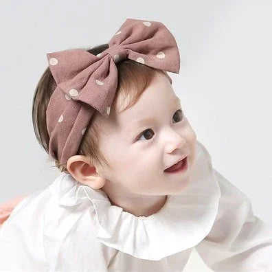 Smiling baby girl wearing a white ruffled collar top and large brown polka dot bow headband