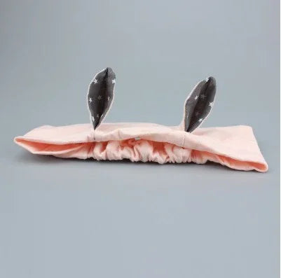 Pink fabric headband with stretchy elastic and gray star-patterned bunny ears on gray background