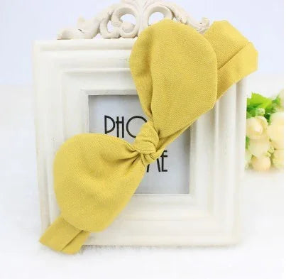 Yellow fabric bow headband displayed on a white ornate photo frame with flowers in the background