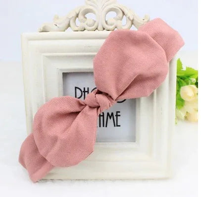 Soft pink fabric headband with a large bow displayed on a decorative white photo frame