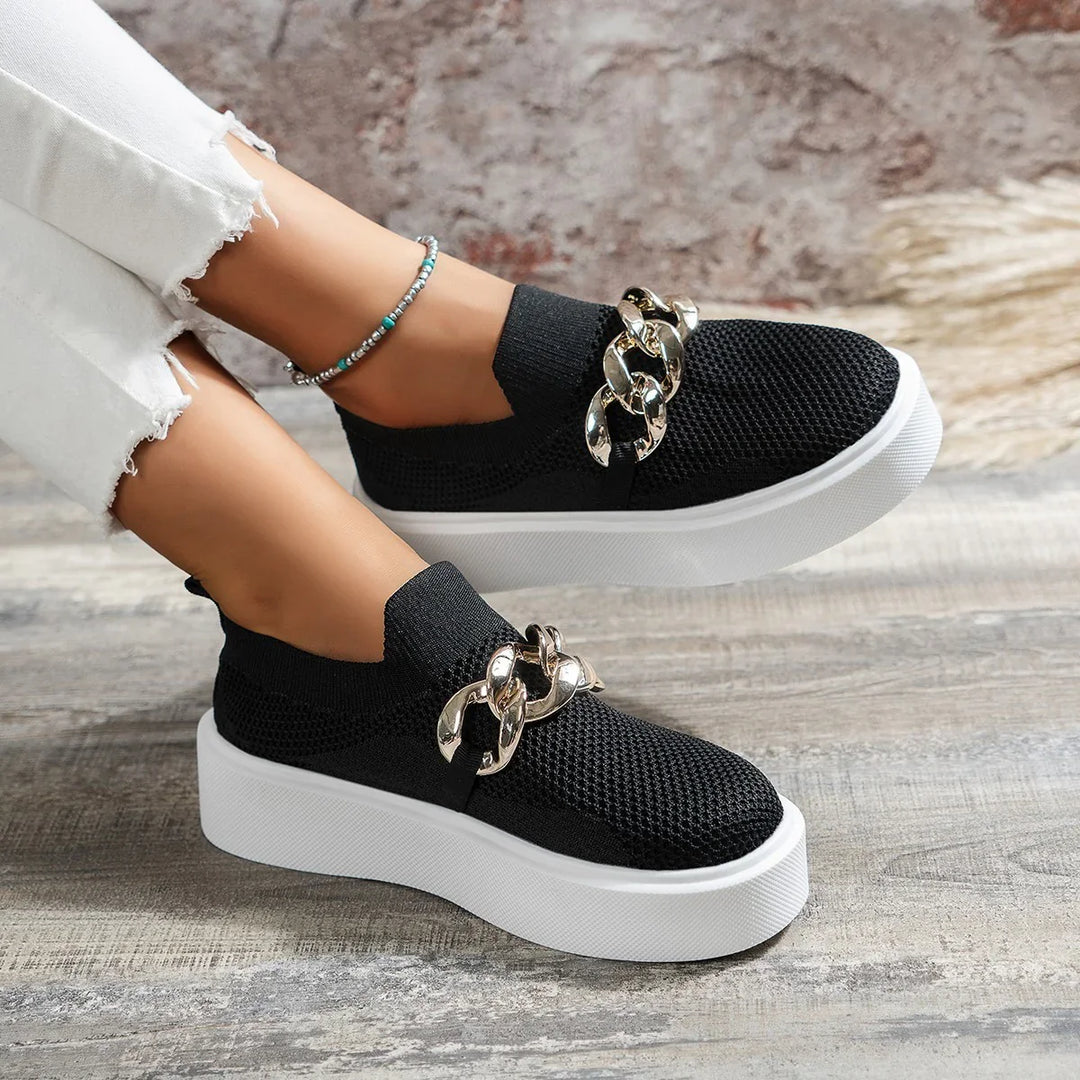 Black slip-on platform sneakers with gold chain detail worn with white distressed jeans